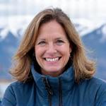 Portrait of Eleanor Vance, a smiling female guide with warm gear and a mountain background.