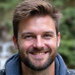 Portrait of Liam O'Connell, a rugged male guide with a friendly smile, by a mountain stream.