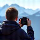 A solo traveler taking a photograph of a mountain vista, while another group member helps frame the shot.
