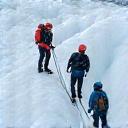 Team of hikers traversing a glacier, roped together for safety with an expert guide.